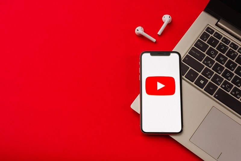 YouTube Cover image - laptop with a smartphone on top with the YouTube logo and wireless earphones